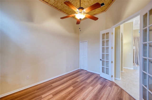 spare room featuring french doors, wood ceiling, light hardwood / wood-style flooring, ceiling fan, and a towering ceiling