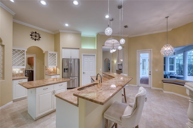 kitchen featuring stainless steel refrigerator with ice dispenser, sink, white cabinetry, hanging light fixtures, and a large island with sink