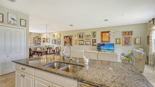 kitchen featuring sink, white cabinetry, an inviting chandelier, hanging light fixtures, and dark stone countertops