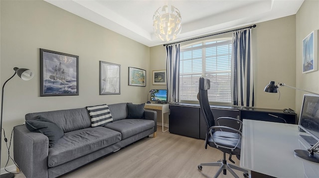 office featuring an inviting chandelier, a tray ceiling, and light hardwood / wood-style floors