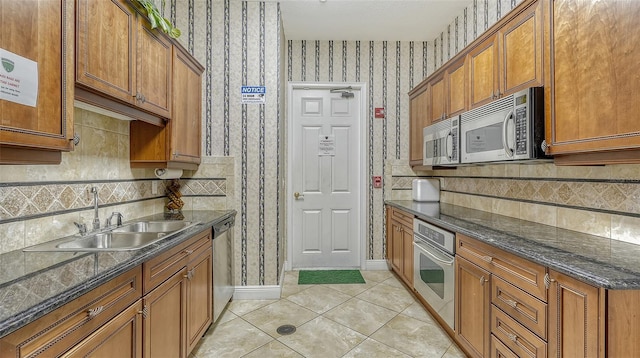 kitchen featuring stainless steel appliances, light tile patterned flooring, sink, and dark stone countertops