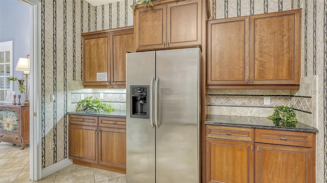 kitchen featuring dark stone counters, stainless steel fridge, decorative backsplash, and light tile patterned floors