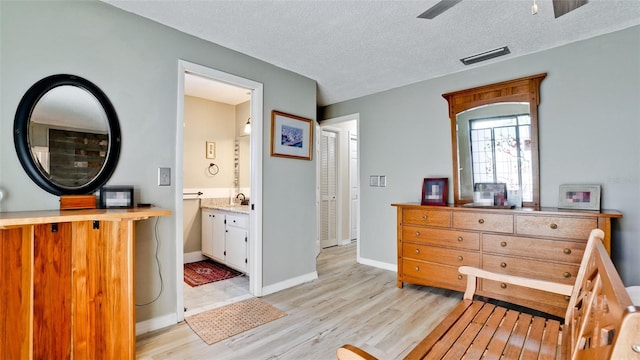 bedroom with ensuite bathroom, light hardwood / wood-style floors, and a textured ceiling