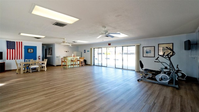 exercise room with crown molding, ceiling fan, wood-type flooring, and a textured ceiling