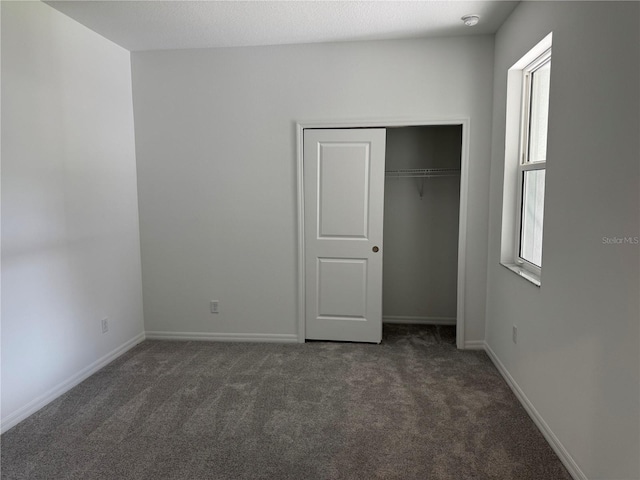 unfurnished bedroom with dark carpet and a closet