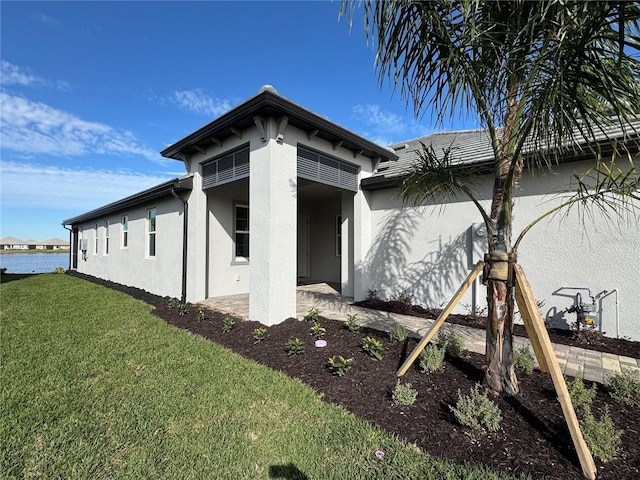 view of side of property with a water view, a patio area, and a lawn