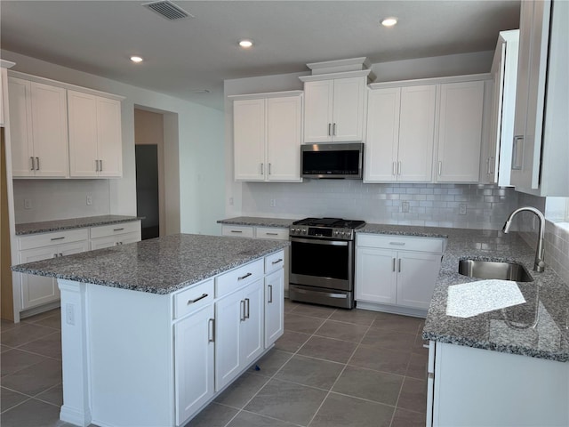 kitchen with sink, appliances with stainless steel finishes, a kitchen island, decorative backsplash, and white cabinets