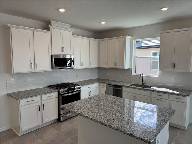 kitchen with sink, white cabinetry, light stone counters, appliances with stainless steel finishes, and a kitchen island