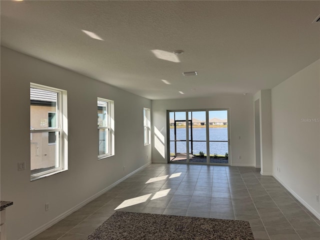 unfurnished room with a textured ceiling, a water view, visible vents, baseboards, and tile patterned floors