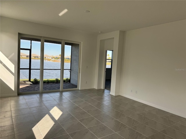 spare room with a water view, baseboards, and dark tile patterned flooring