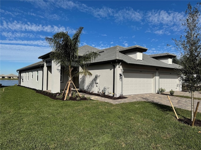 view of side of property with a garage, decorative driveway, a yard, and stucco siding