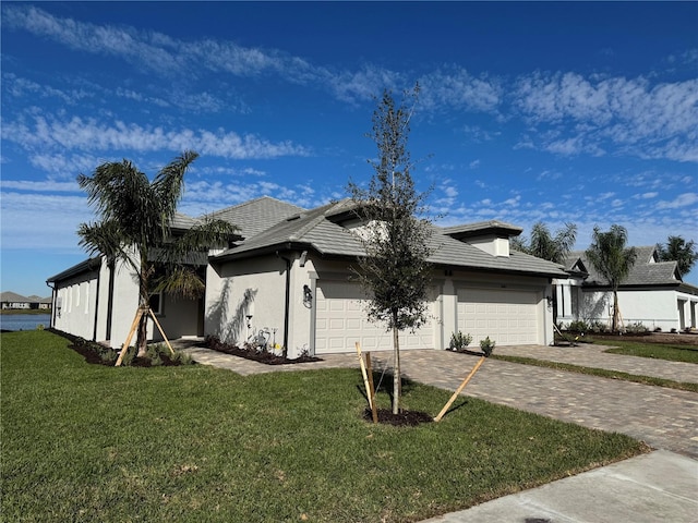 view of front of property featuring decorative driveway, an attached garage, a front lawn, and stucco siding