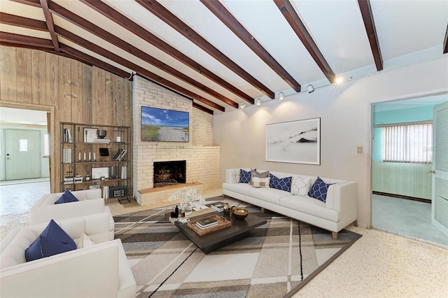 living room with high vaulted ceiling, wood walls, beamed ceiling, a brick fireplace, and track lighting