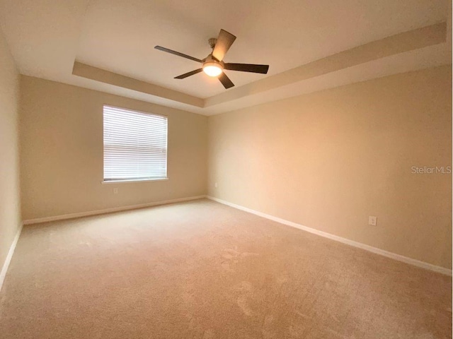 carpeted spare room featuring ceiling fan and a tray ceiling