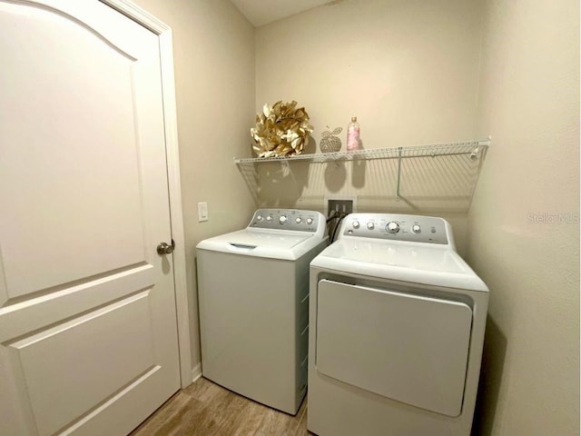 clothes washing area with washing machine and dryer and light wood-type flooring