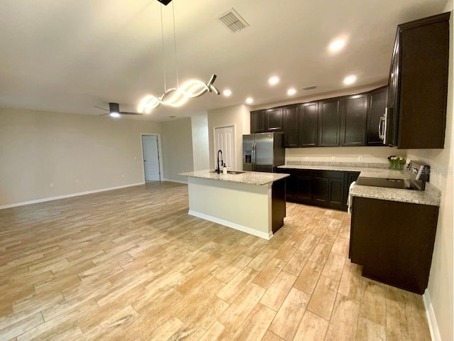 kitchen with pendant lighting, stove, a kitchen island with sink, light stone counters, and stainless steel fridge with ice dispenser