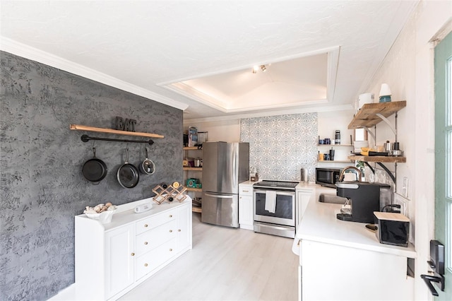 kitchen with stainless steel appliances, a tray ceiling, ornamental molding, white cabinets, and light wood-type flooring