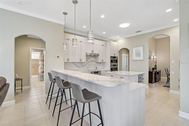 kitchen featuring a kitchen bar, decorative light fixtures, kitchen peninsula, stainless steel double oven, and white cabinets