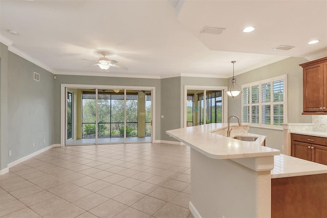 kitchen with sink, hanging light fixtures, a kitchen island with sink, light tile patterned floors, and crown molding