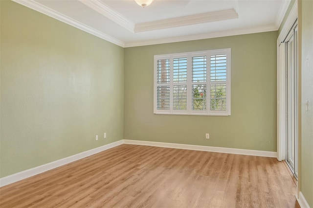 unfurnished bedroom with crown molding, a tray ceiling, a closet, and light wood-type flooring