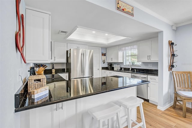 kitchen with stainless steel appliances, white cabinets, a kitchen bar, and a tray ceiling