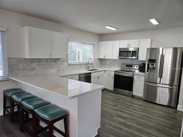 kitchen featuring sink, appliances with stainless steel finishes, white cabinets, a kitchen bar, and kitchen peninsula