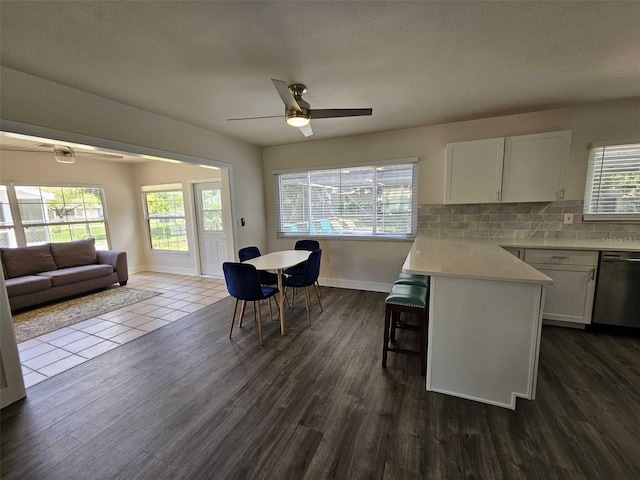 kitchen with a breakfast bar, white cabinetry, dishwasher, backsplash, and dark wood-type flooring