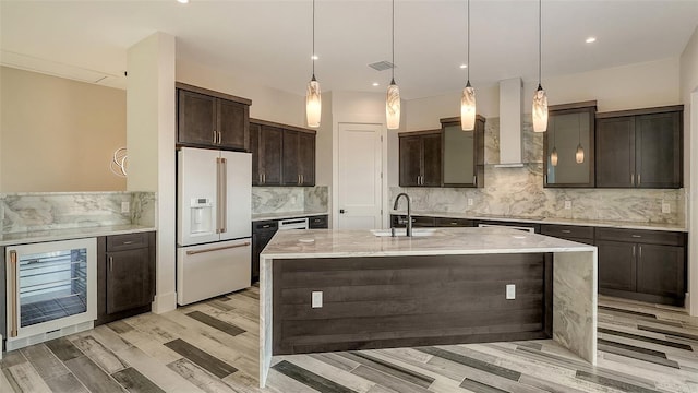 kitchen featuring dark brown cabinetry, high end fridge, decorative light fixtures, beverage cooler, and wall chimney range hood