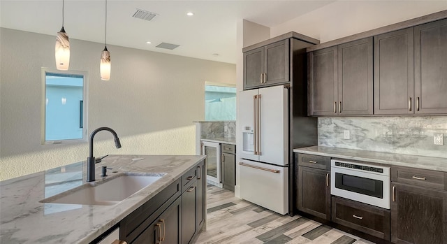 kitchen with decorative light fixtures, high end white refrigerator, sink, light stone countertops, and dark brown cabinets