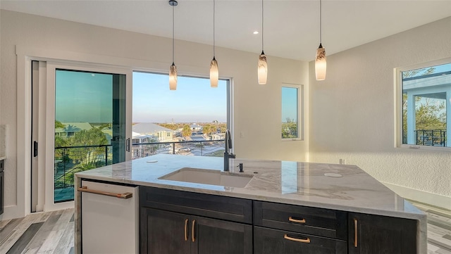 kitchen featuring sink, hanging light fixtures, light stone countertops, a center island with sink, and light wood-type flooring