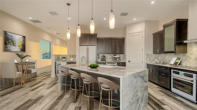 kitchen featuring a kitchen island, built in refrigerator, light stone counters, white oven, and dark brown cabinets