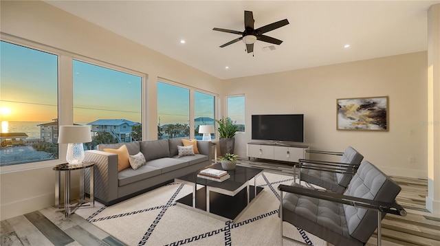 living room with ceiling fan, a water view, and light wood-type flooring