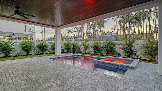 pool at dusk with an in ground hot tub, ceiling fan, and a patio