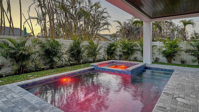 pool at dusk with an in ground hot tub