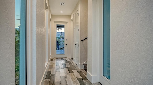 corridor featuring a textured wall, wood finished floors, and visible vents