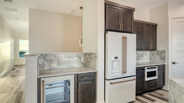 kitchen with white appliances, beverage cooler, tasteful backsplash, dark brown cabinets, and light wood-style floors