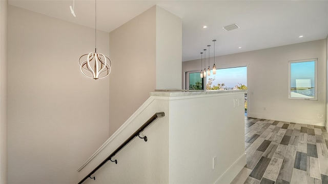 hallway featuring visible vents, baseboards, an upstairs landing, light wood finished floors, and an inviting chandelier