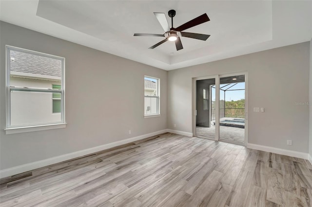 unfurnished room with ceiling fan, a tray ceiling, and light wood-type flooring