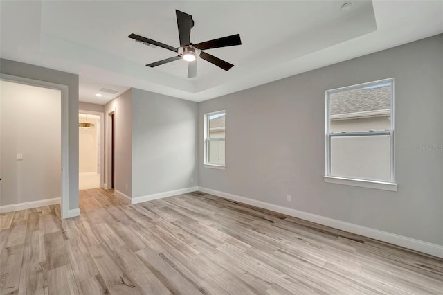 spare room with a raised ceiling, ceiling fan, and light hardwood / wood-style flooring