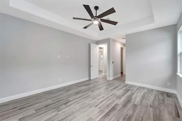 unfurnished bedroom featuring a tray ceiling, ceiling fan, and light wood-type flooring