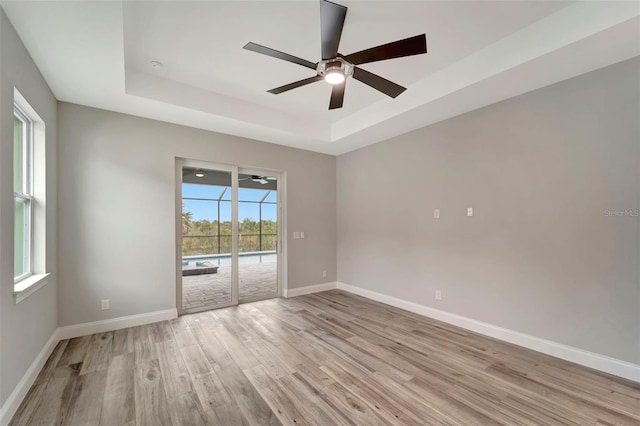 empty room featuring light hardwood / wood-style flooring, ceiling fan, and a tray ceiling