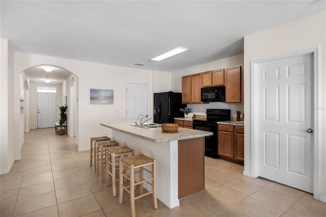 kitchen featuring light tile patterned floors, a breakfast bar, an island with sink, and black appliances