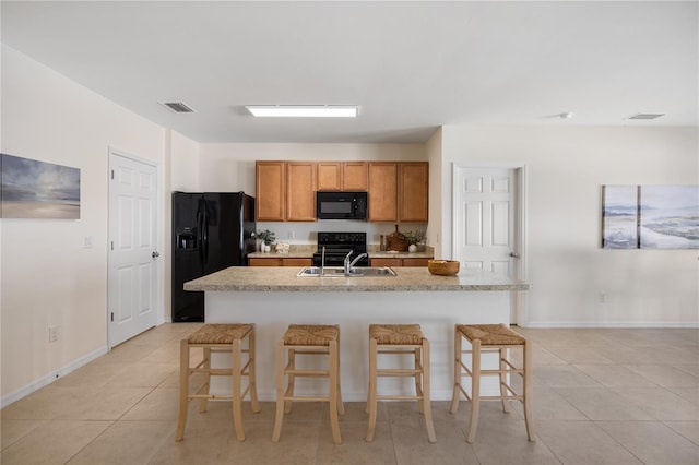 kitchen featuring a breakfast bar, a center island with sink, and black appliances