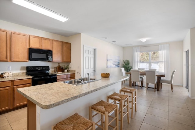 kitchen featuring sink, light tile patterned floors, a breakfast bar area, black appliances, and a center island with sink