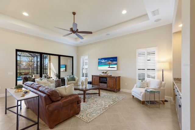 tiled living room with a tray ceiling, ceiling fan, and a high ceiling