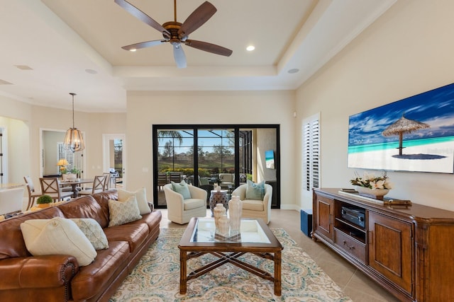 tiled living room with a towering ceiling, a raised ceiling, and ceiling fan with notable chandelier