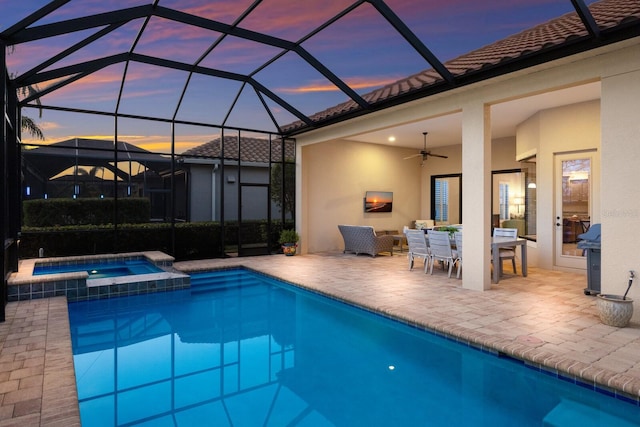 pool at dusk with a lanai, a patio area, ceiling fan, and an in ground hot tub