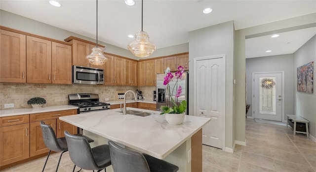 kitchen featuring appliances with stainless steel finishes, sink, an island with sink, and hanging light fixtures