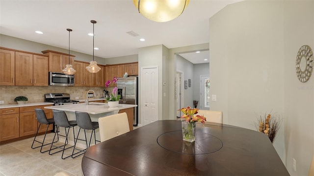 kitchen with hanging light fixtures, an island with sink, appliances with stainless steel finishes, and backsplash