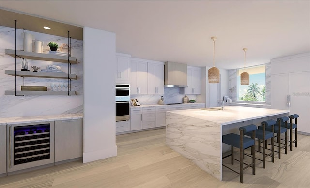 kitchen featuring hanging light fixtures, white cabinetry, wall chimney range hood, and beverage cooler